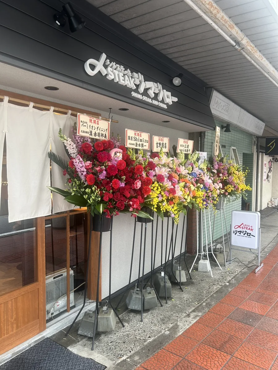 店舗立ち上げ支援を行ったステーキ店の外観。店舗看板と開店祝いの花が並ぶ様子